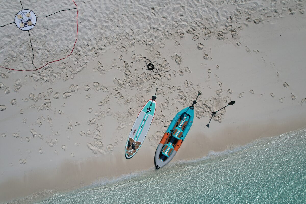 Paddleboard and kayak on pale sand beside clear water